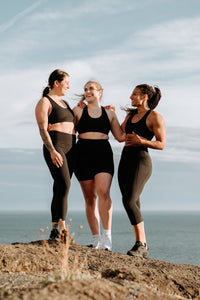 Three women standing on a rocky cliff looking happy with the ocean behind them