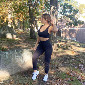 A woman standing in a backyard wearing black activewear and looking ready for a run