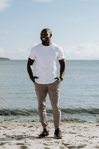 A man wearing shark heather joggers and a white shirt standing on the beach in front of the ocean