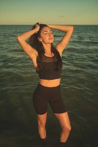 A woman standing in the ocean wearing bike shorts and a mesh sports top bra