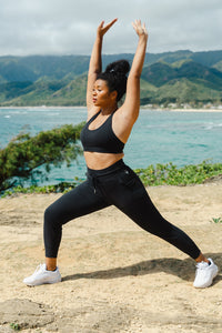 A woman stretching next to the ocean with mountains behind her