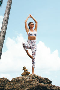 A woman standing on a rock in a balancing yoga pose with her foot on her knee and her hands above her head