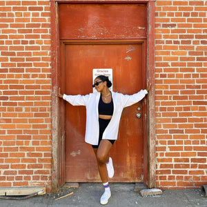 A woman standing in a doorway next to a brick wall wearing onyx bike shorts and contrast bra