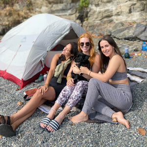 Three women and a small dog sitting outside of a tent wearing seaav apparel
