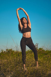 A woman standing in a field and stretching her arms above her head